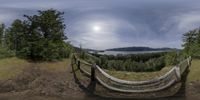 a 360 - camera photo of the ocean, mountains and trees in front of a fence