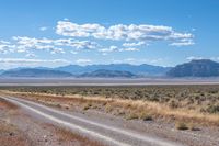 road leading through desert area with clouds in the distance and mountains on either side of it