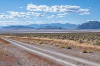 road leading through desert area with clouds in the distance and mountains on either side of it