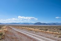 road leading through desert area with clouds in the distance and mountains on either side of it