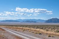 road leading through desert area with clouds in the distance and mountains on either side of it