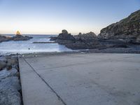 a pier with a surfboard on it near the ocean and rocky shore with rocks in the water