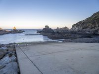 a pier with a surfboard on it near the ocean and rocky shore with rocks in the water