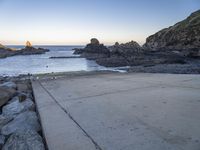 a pier with a surfboard on it near the ocean and rocky shore with rocks in the water