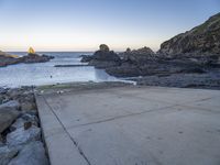 a pier with a surfboard on it near the ocean and rocky shore with rocks in the water