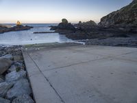 a pier with a surfboard on it near the ocean and rocky shore with rocks in the water