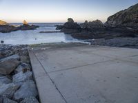 a pier with a surfboard on it near the ocean and rocky shore with rocks in the water