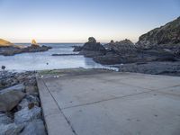 a pier with a surfboard on it near the ocean and rocky shore with rocks in the water