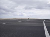 a highway with clouds and dirt in the background as a single car sits on the pavement