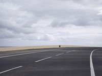 a highway with clouds and dirt in the background as a single car sits on the pavement