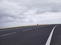 a highway with clouds and dirt in the background as a single car sits on the pavement