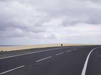 a highway with clouds and dirt in the background as a single car sits on the pavement