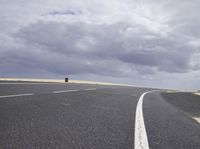 a highway with clouds and dirt in the background as a single car sits on the pavement