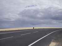 a highway with clouds and dirt in the background as a single car sits on the pavement