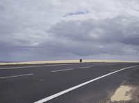 a highway with clouds and dirt in the background as a single car sits on the pavement