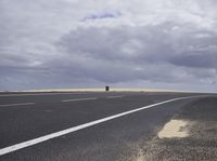 a highway with clouds and dirt in the background as a single car sits on the pavement