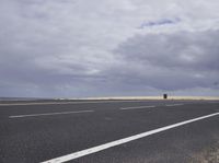 a highway with clouds and dirt in the background as a single car sits on the pavement