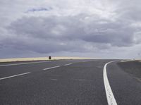 a highway with clouds and dirt in the background as a single car sits on the pavement