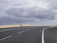 a highway with clouds and dirt in the background as a single car sits on the pavement