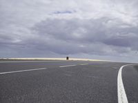 a highway with clouds and dirt in the background as a single car sits on the pavement