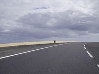 a highway with clouds and dirt in the background as a single car sits on the pavement