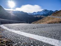 an asphalt highway stretches into the mountains, with a lone man standing by the roadside