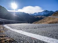 an asphalt highway stretches into the mountains, with a lone man standing by the roadside