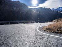 an asphalt highway stretches into the mountains, with a lone man standing by the roadside
