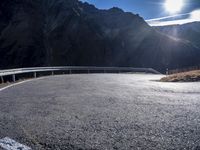 an asphalt highway stretches into the mountains, with a lone man standing by the roadside