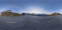 a wide angle panoramic view of a highway near snow capped mountains and a red building