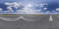 a wide photo of a highway with many markings on it and lots of white clouds