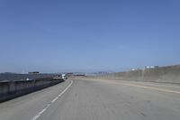 cars on a highway next to a large bridge with a lake and blue sky in the background