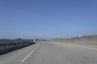 cars on a highway next to a large bridge with a lake and blue sky in the background