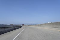 cars on a highway next to a large bridge with a lake and blue sky in the background