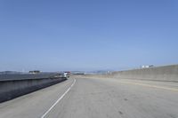 cars on a highway next to a large bridge with a lake and blue sky in the background