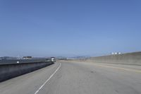 cars on a highway next to a large bridge with a lake and blue sky in the background