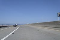 cars on a highway next to a large bridge with a lake and blue sky in the background