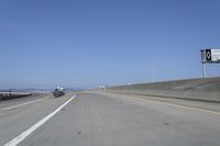 cars on a highway next to a large bridge with a lake and blue sky in the background