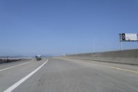 cars on a highway next to a large bridge with a lake and blue sky in the background