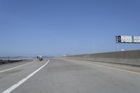 cars on a highway next to a large bridge with a lake and blue sky in the background