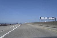 cars on a highway next to a large bridge with a lake and blue sky in the background