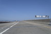 cars on a highway next to a large bridge with a lake and blue sky in the background