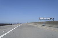 cars on a highway next to a large bridge with a lake and blue sky in the background