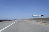 cars on a highway next to a large bridge with a lake and blue sky in the background