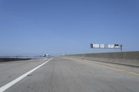 cars on a highway next to a large bridge with a lake and blue sky in the background