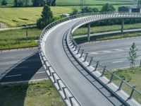 a curved road leading through a rural countryside area with highway traffic in the distance against a blue sky