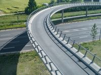 a curved road leading through a rural countryside area with highway traffic in the distance against a blue sky