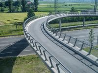 a curved road leading through a rural countryside area with highway traffic in the distance against a blue sky