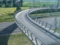 a curved road leading through a rural countryside area with highway traffic in the distance against a blue sky