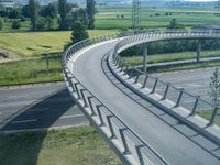 a curved road leading through a rural countryside area with highway traffic in the distance against a blue sky